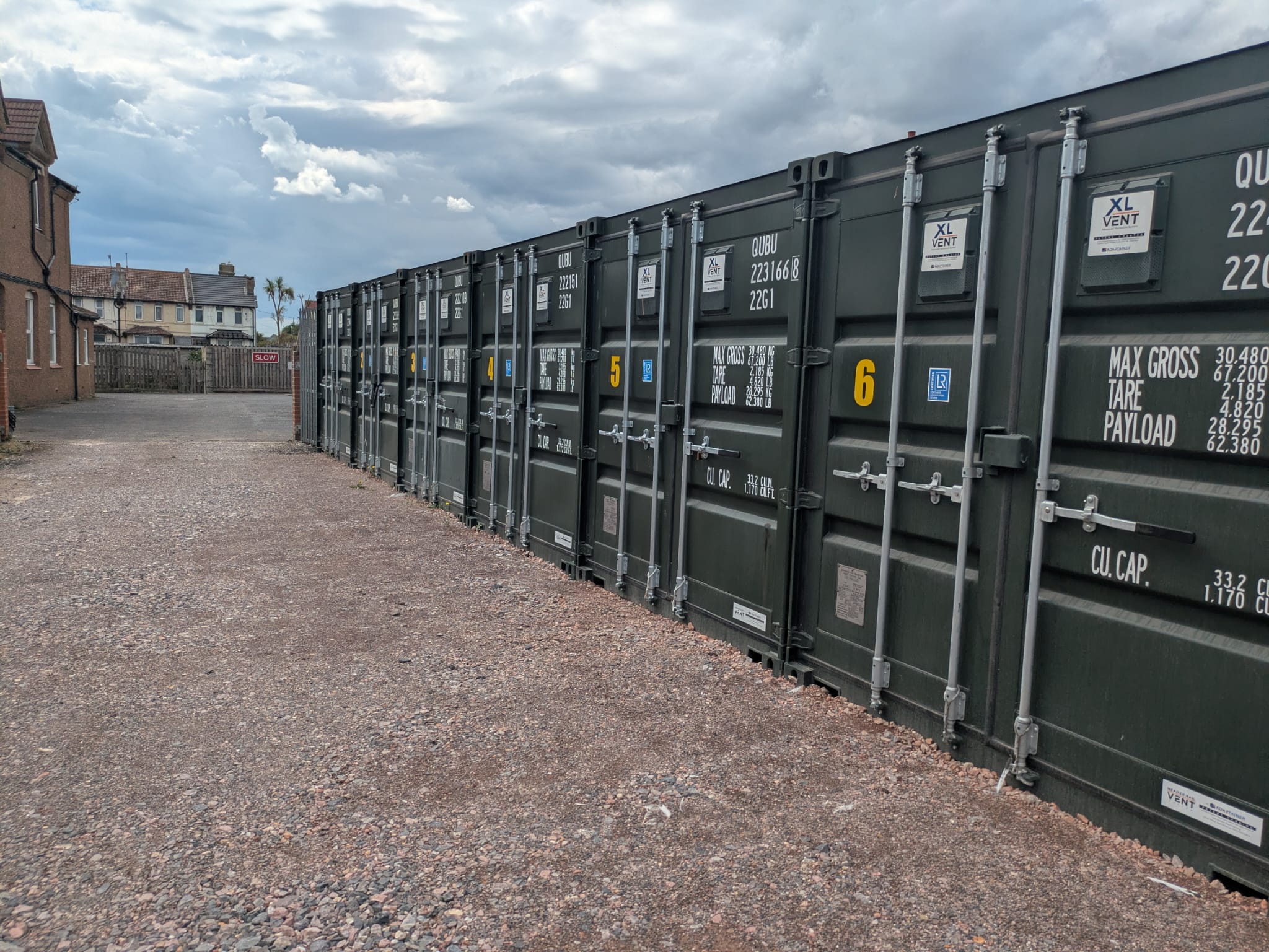 A long row of secure blue 20ft self-storage containers on a gravel yard